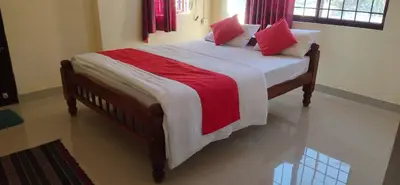 a large bed with red and white sheets and pillows at Shanthala Residency in Virajpet