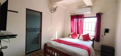 a bedroom with a bed with red curtains and a window at Shanthala Residency in Virajpet
