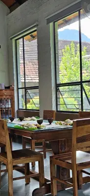 a dining room with a table and chairs and windows at Pannadikadu Homestay in Sethumadai