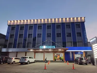 a building with cars parked in front of it at Georjoys Hotels & Resorts in Kalpetta