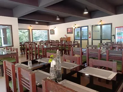 a restaurant with wooden tables and chairs and windows at Milife Medicity Perashannoor in Kuttippuram
