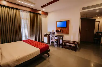 a bedroom with a bed and a table and a television at Nirmallyam Residency Hotel in Edappāl
