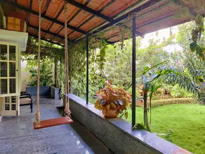 a porch with a porch swing and a vase of flowers at Garden Home mindfully laid out & furnished in Mysore