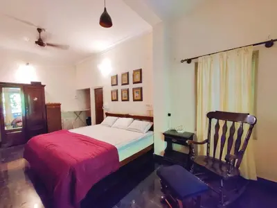 a bedroom with a bed with a red blanket and a chair at Garden Home mindfully laid out & furnished in Mysore
