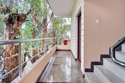 a balcony with stairs and a large tree at Super Hotel O Rose Garden Ooty Formerly New Star Cottages in Ooty