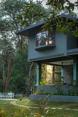 a blue house with a balcony in a yard at Coorg Wild Walk, Nagarhole - A CGH Earth SAHA Experience in Srimangala