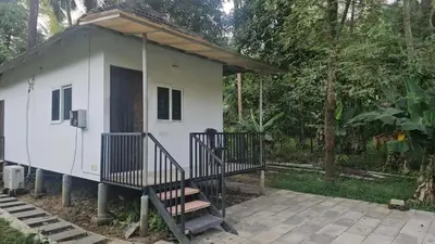 a small white tiny house with a porch and stairs at Nila Organica Farm Stay in Palakkad