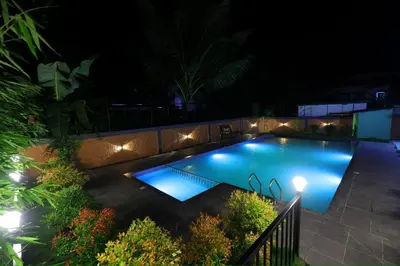 a swimming pool lit up at night with lights at sky blue villa in Vythiri