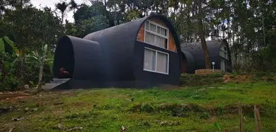 a small black house on a grassy field at Ginberry Holidays in Wayanad