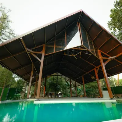 a building with a roof over a swimming pool at Ohstayz Villa De Estate 64 in Kizhake Chālakudi