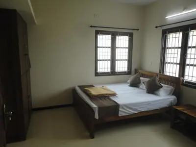 a bedroom with a bed with white sheets and two windows at Sanvika Hotels & Service Apartments in Coimbatore