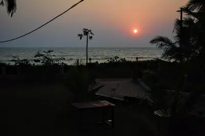 a sunset on the beach with a table and palm trees at Club 7 Beach Resort in Kannur