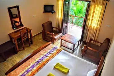 a bedroom with a bed and chairs and a balcony at Club 7 Beach Resort in Kannur
