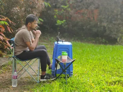 a man sitting in a chair next to a blue suitcase at Mysticgreens Home Stay in Piriyāpatna