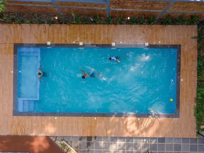 three people swimming in a large swimming pool at Swastha Royal Resort Wayanad in Kaniyāmbetta