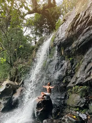 a man sitting on a rock in front of a waterfall at Nomadcasa Rooms in Kanthalloor