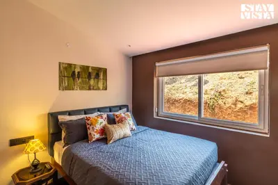 a bedroom with a blue bed and a window at StayVista at Valley Whispers with BBQ & Bonfire in Ooty