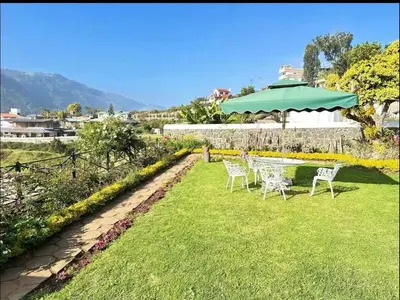 a table and chairs on a lawn with a green umbrella at Ivy Cottage Kodaikanal in Kodaikānāl