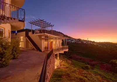 a house on a hill with the sunset in the background at Central Homestay Ooty by VOYE HOMES Family-Friendly Budget Stay with Valley And Mountain Views in Ooty