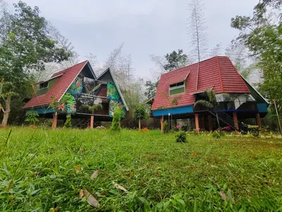 two houses with red roofs in a field at River Valley Huts, Wayanad in Panamaram