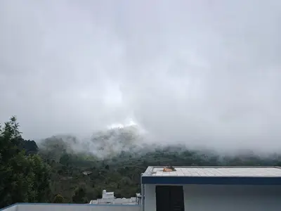a mountain obscured by clouds with a house in the foreground at Jazz&Hill in Kodaikānāl