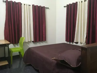 a bedroom with red curtains and a green chair at Peaceful perch in Kozhikode