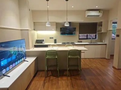 a kitchen with two bar chairs and a large screen tv at Gulzar 1BHK Service Apartment, kannur in Kannur