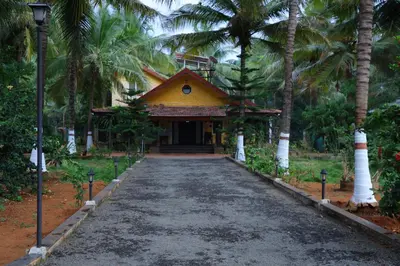 a road leading to a yellow building with palm trees at SS Farms By Shivalaya Stays in Alāndurai