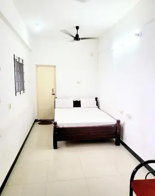 a bedroom with a bed in a white room at PALLIYARAI GARDENS LODGE AND HOMESTAy in Palani