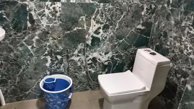 a bathroom with a white toilet and a marble wall at Ammavvana Kutira Home stay in Madikeri