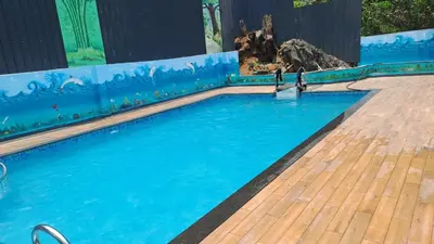 a swimming pool with blue water and a wooden deck at Natura Homestay in Padinjarathara