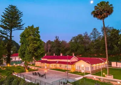 a large building with a red roof in a park at Mowbray House Resort Ooty by VOYE HOMES in Ooty