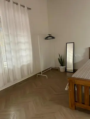 a living room with a wooden floor and white curtains at Airy haven in Kushālnagar