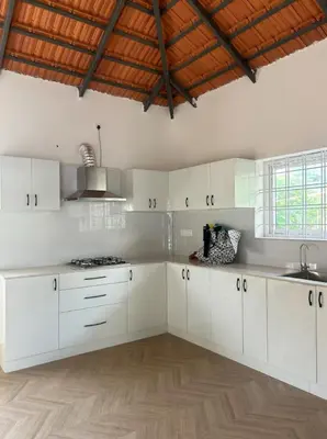 a kitchen with white cabinets and a wooden floor at Airy haven in Kushālnagar