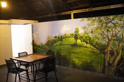 a table and chairs in front of a wall with a painting at Fog Land Pool Villa by BMT in Vythiri