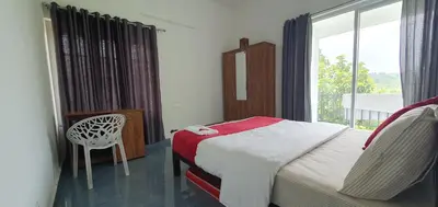 a bedroom with a bed and a chair and a window at Parthees Homestay in Meppādi