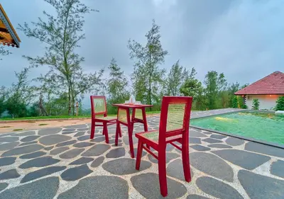 two red chairs and a table on a patio at Whispering Hills Pine Malhar Pool & Tent Attappadi by VOYE HOMES in Attappādi