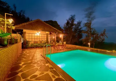 a swimming pool in front of a house at night at Whispering Hills Pine Malhar Pool & Tent Attappadi by VOYE HOMES in Attappādi
