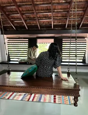 a woman sitting on a table looking out a window at SaffronStays Amaya - 5BR 300-year-old Kerala-style heritage villa with spa near Kannur Airport in Irikkūr