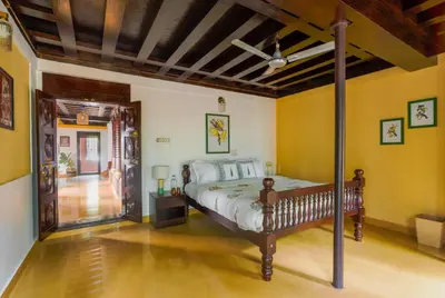 a bedroom with a bed in a room with yellow walls at SaffronStays Amaya - 5BR 300-year-old Kerala-style heritage villa with spa near Kannur Airport in Irikkūr