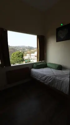 a bedroom with a bed and a large window at Mira Homestay in Kodaikānāl