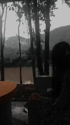 a woman sitting at a table looking out at a river at Rainy Woods Inn in Neriyamangalam
