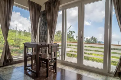 a room with large windows and a table and chairs at The Misty Meadows in Coonoor