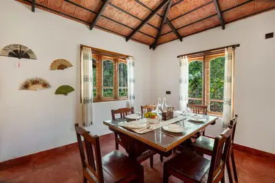 a dining room with a table and chairs and windows at Sliceinn Somewhere Together In Biligeri in Madikeri