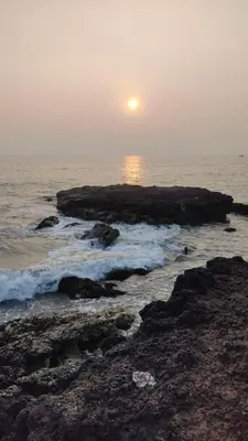 a sunset over the ocean with rocks in the water at Peaceful Homestay near Kizhunna Beach in Thottada