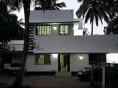 a white house with a car parked in front of it at Anand Bagh in Pollāchi