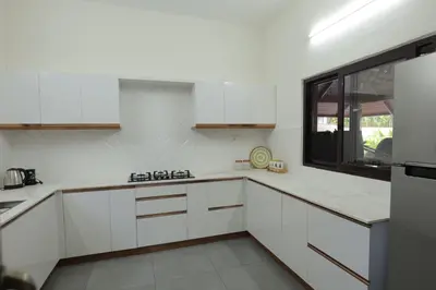 a white kitchen with white cabinets and a window at Kaayal Experience - Entire Home in Kozhikode in Kozhikode