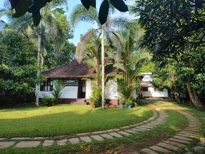 a house with palm trees in front of a yard at The Mangosteen Homestay in Kodanad
