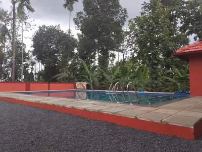a swimming pool with a red fence and trees at Empire Life Pool Villa in Meenangadi