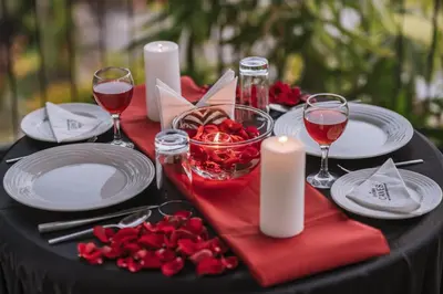 a black table with white plates and candles and red flowers at EVORA Resort and SPA in Ambalavayal